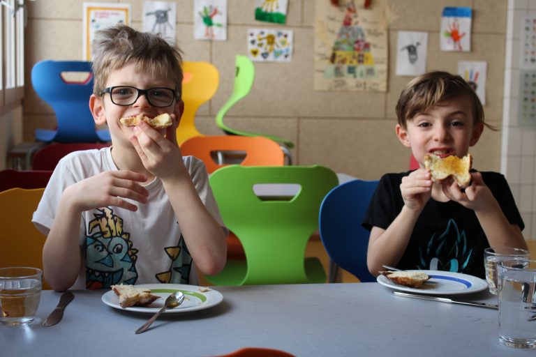 Kinder der Nachmittagsbetreuung essen selbstgemachte Schmetterlingsbroetchen